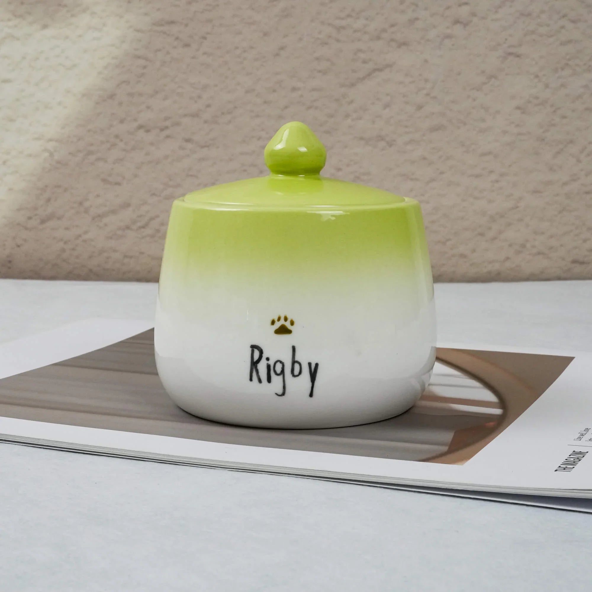 Green and white ceramic jar with 'Rigby' on a textured surface