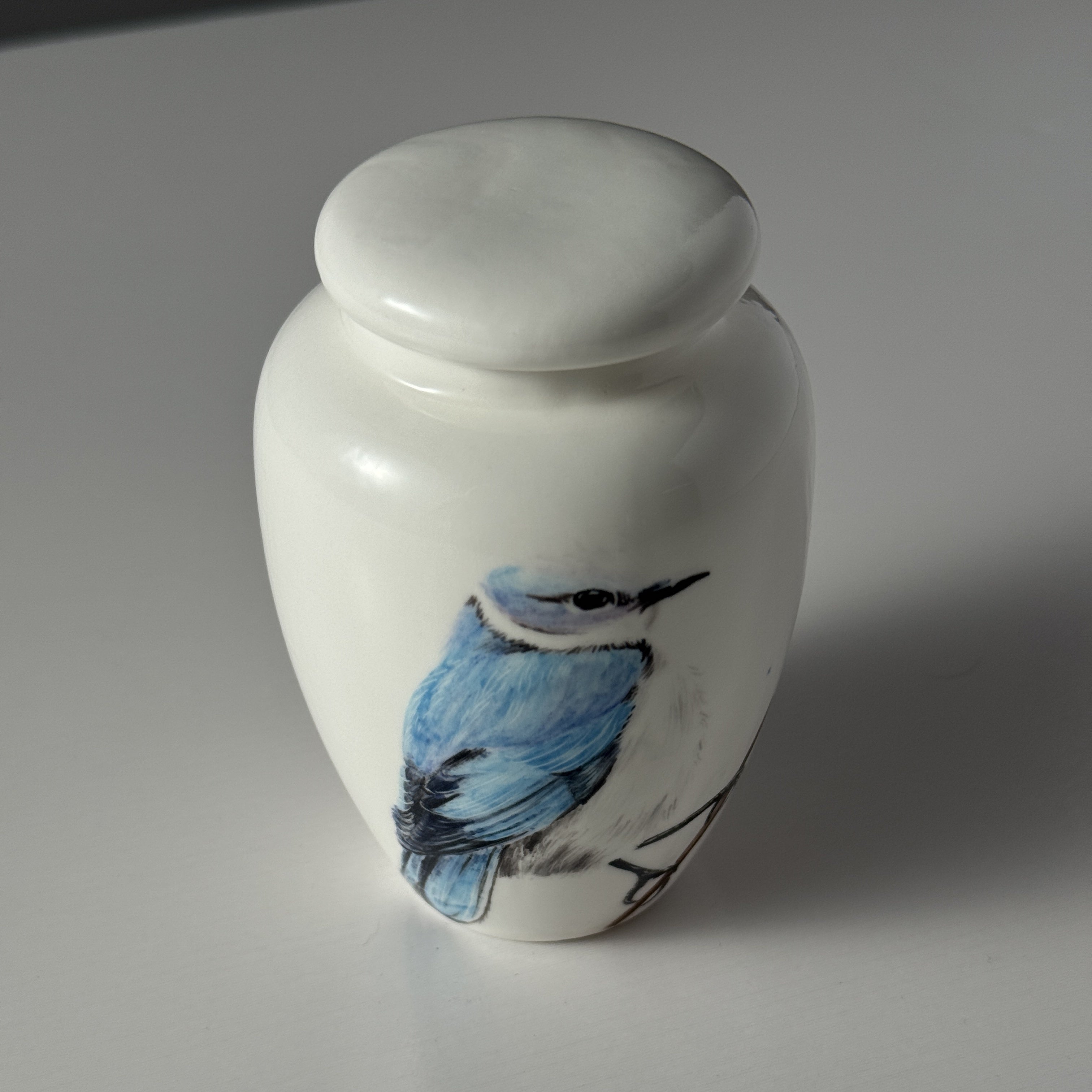 White urn with a blue bird design on a gray background