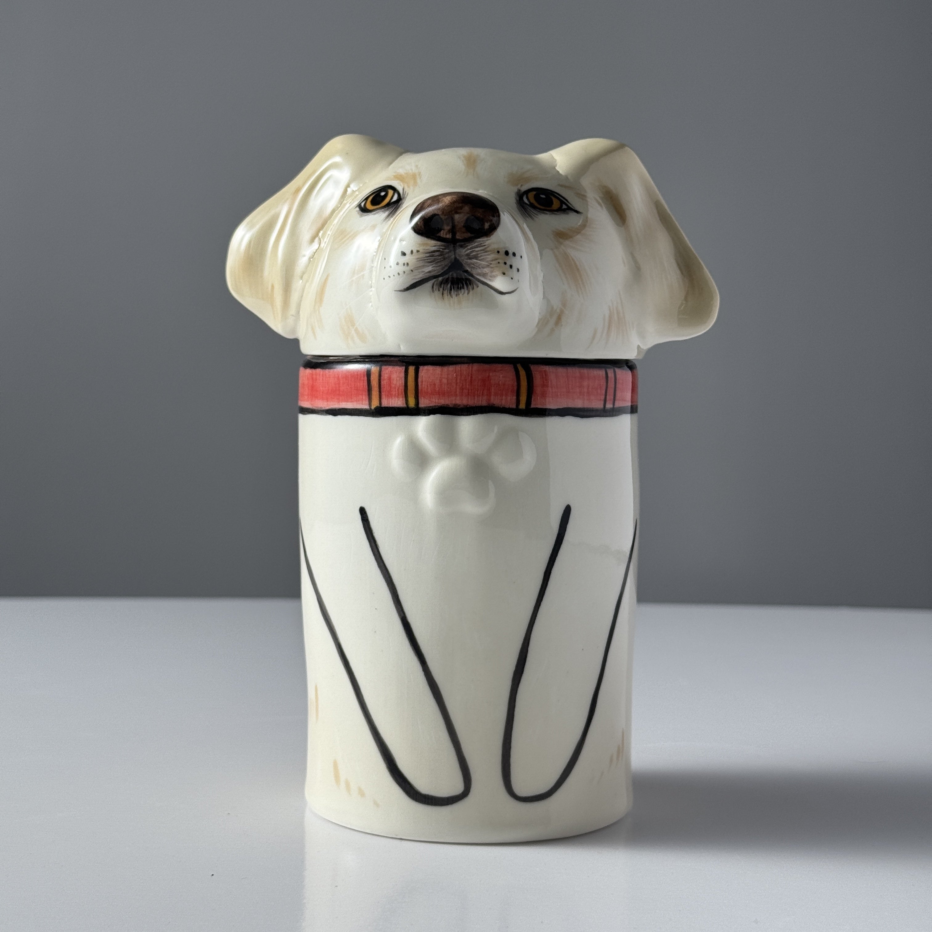 Ceramic jar shaped like a dog with a plaid collar on a gray background