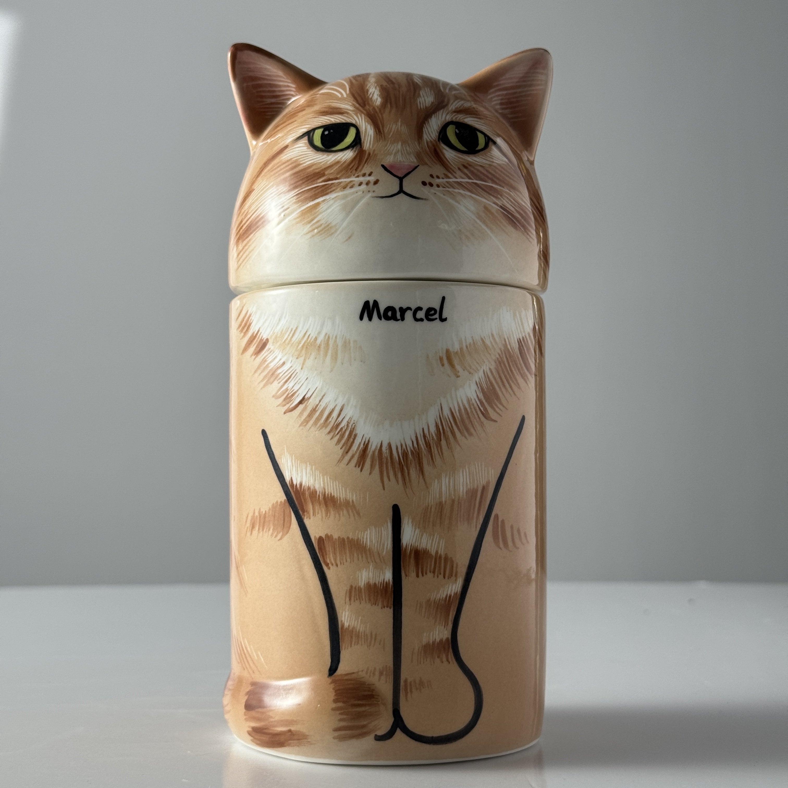 Cat-shaped ceramic jar with 'Marcel' on a white background