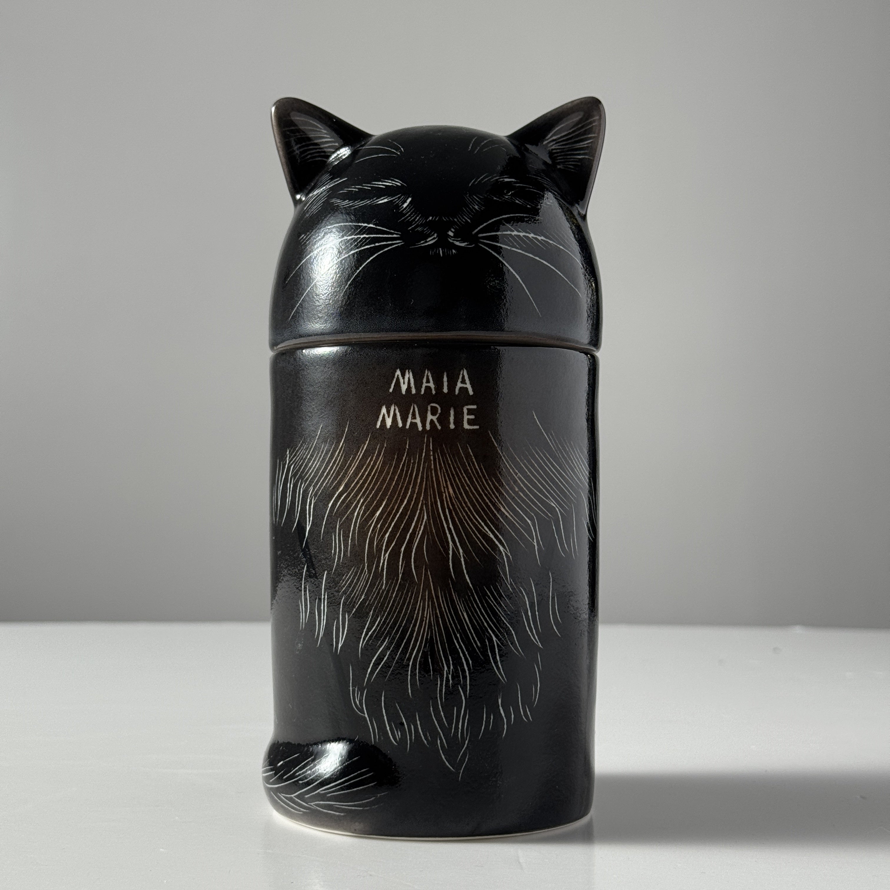 Black cat-shaped container with 'MAIA MARIE' branding on a gray background