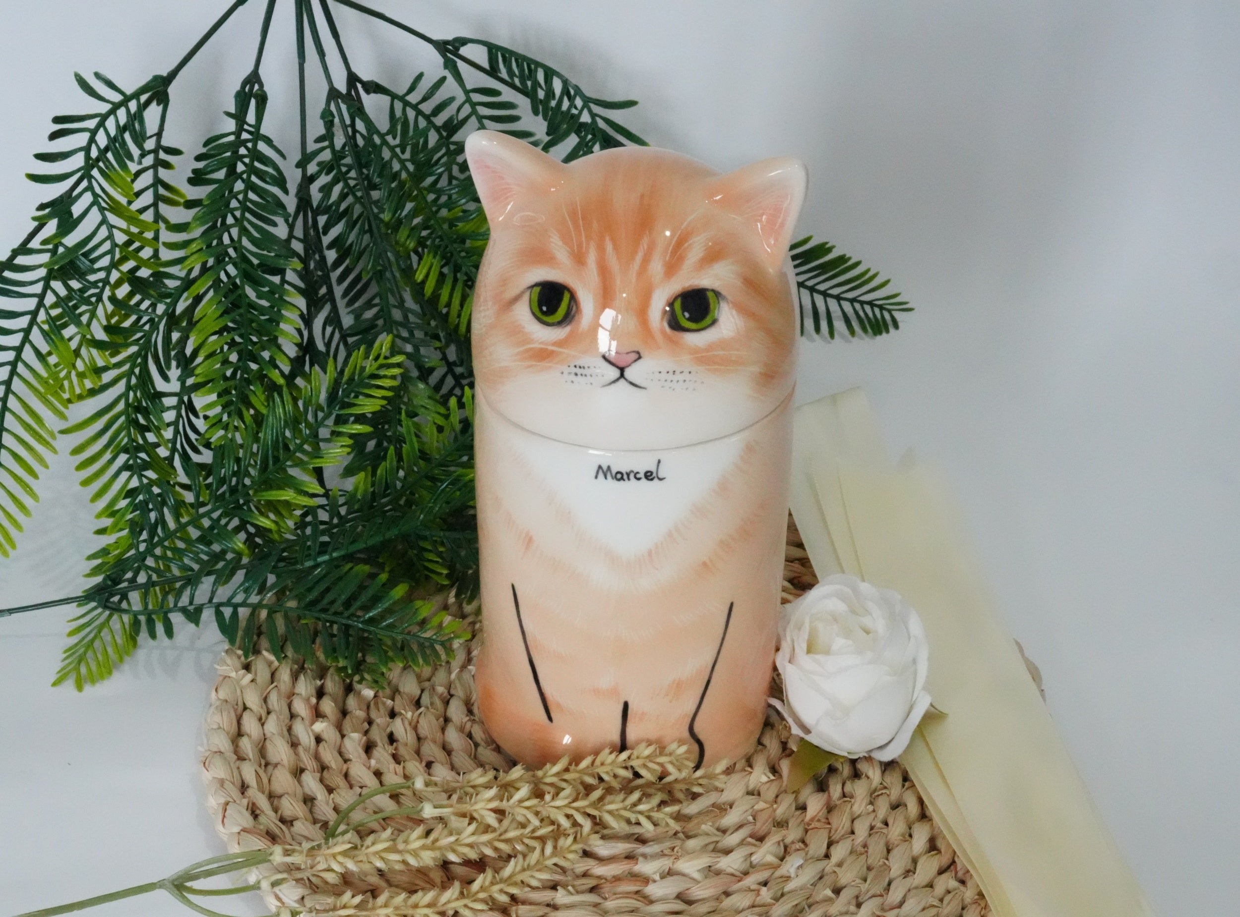 Cat-shaped ceramic mug with 'Marcel' on a textured surface with greenery and a white flower.