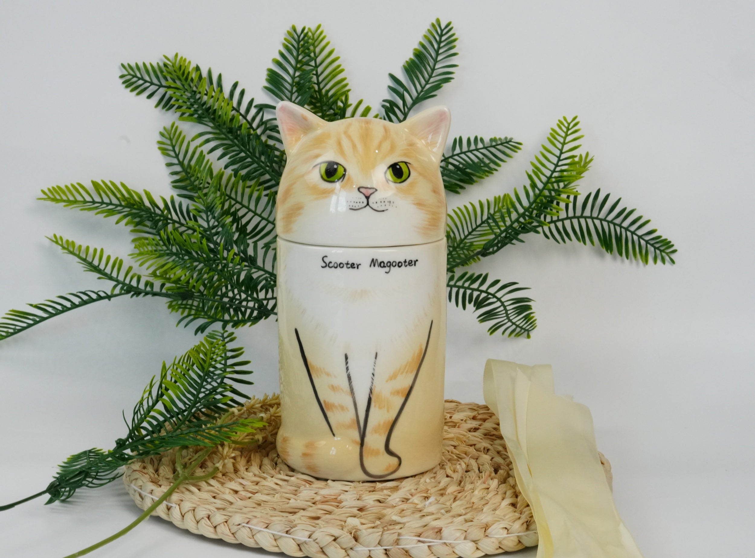 Cat-shaped candle with 'Scooter Nagoya' text, surrounded by green leaves on a white background