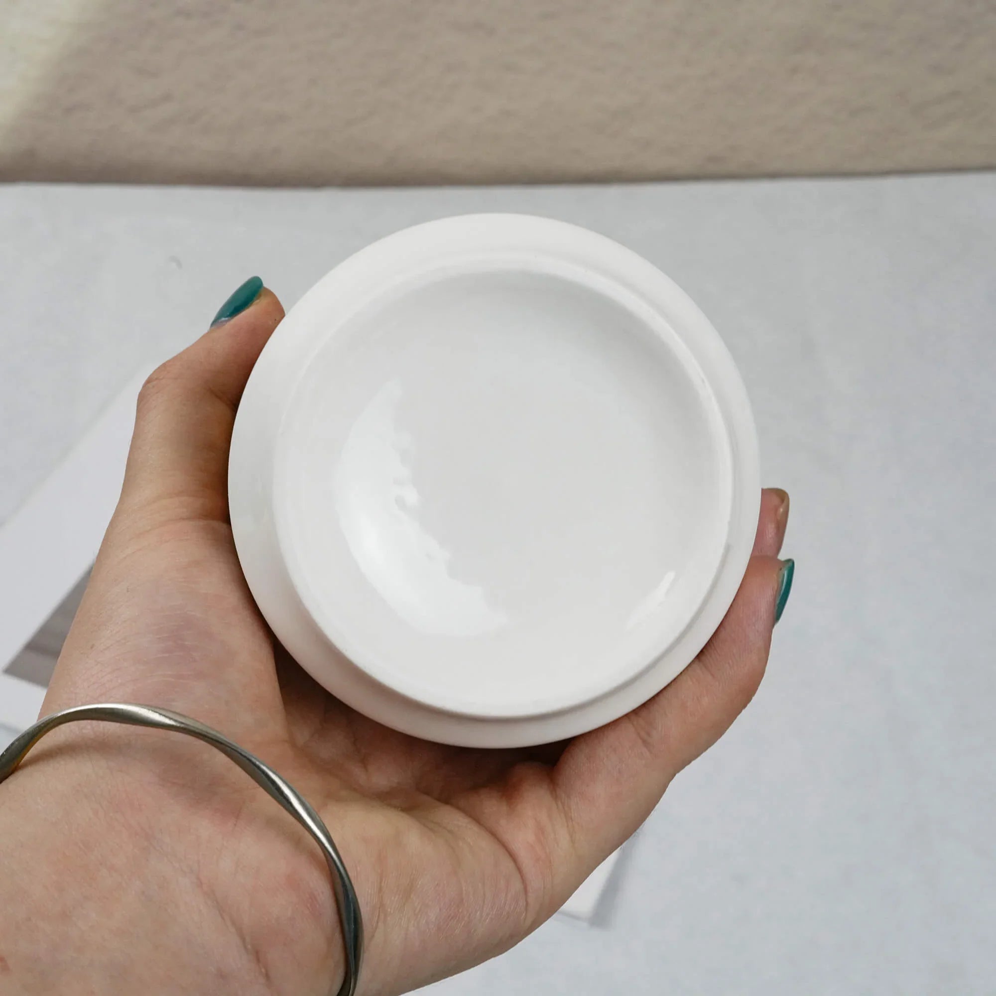 Hand holding a white jar lid against a neutral background