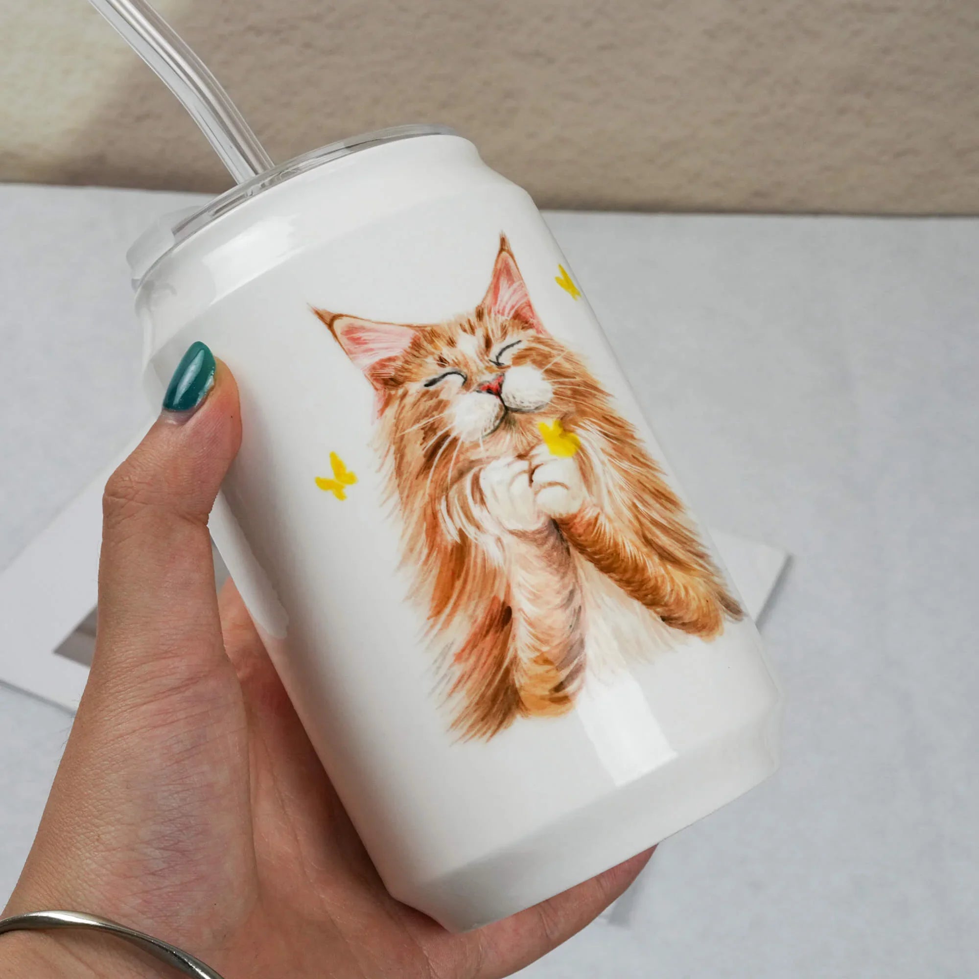 White tumbler with a cat design held by a hand on a light gray background
