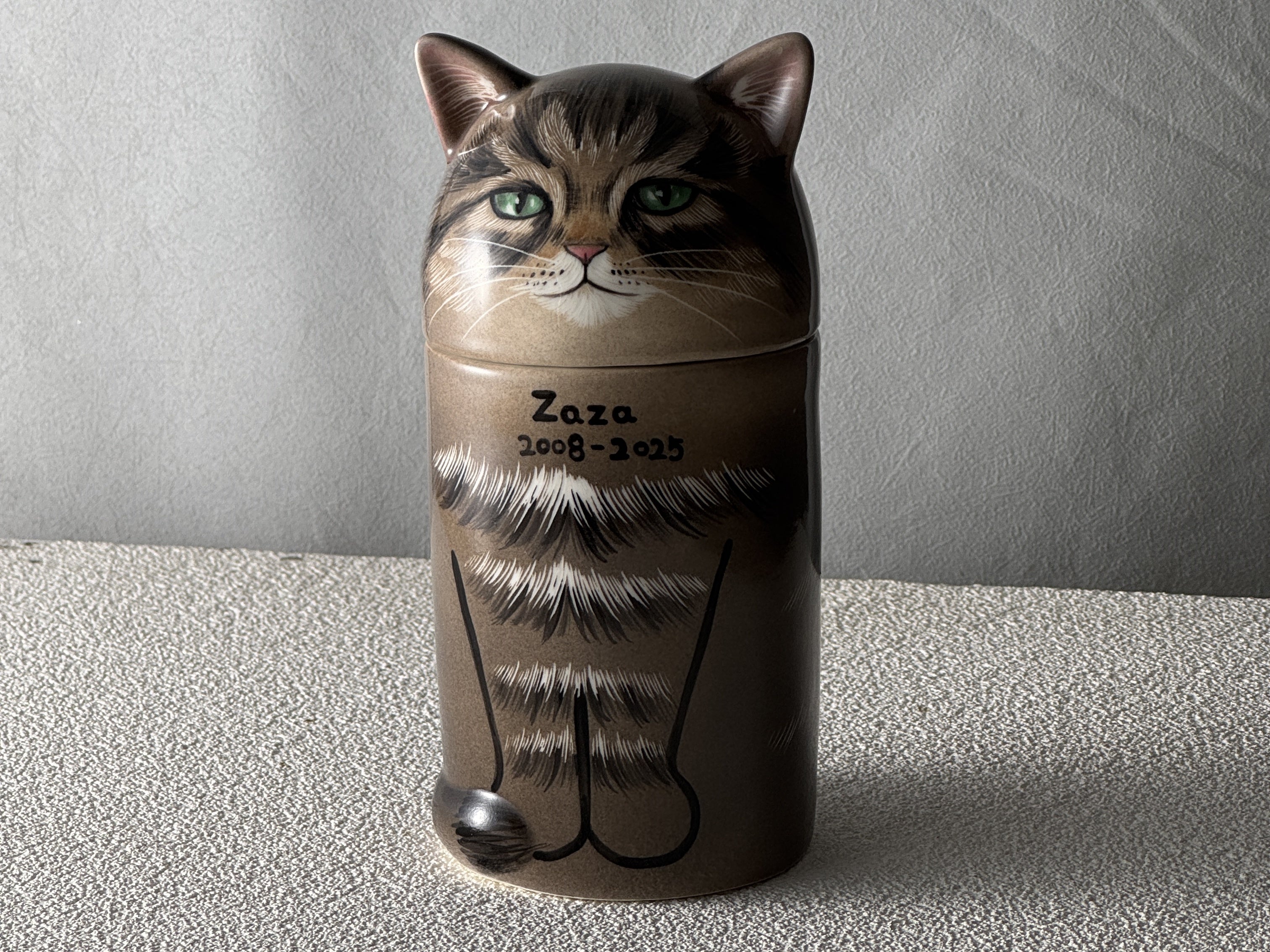 Cat-shaped urn with 'Zaza' and a date on a neutral background