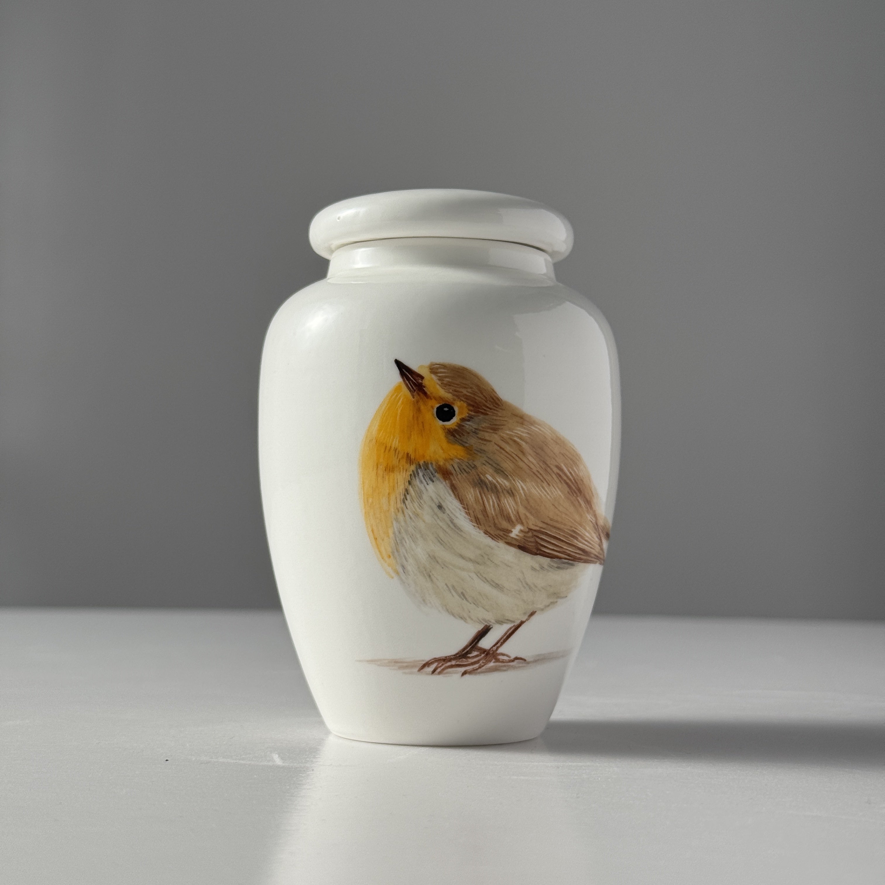 White urn with a robin design on a gray background