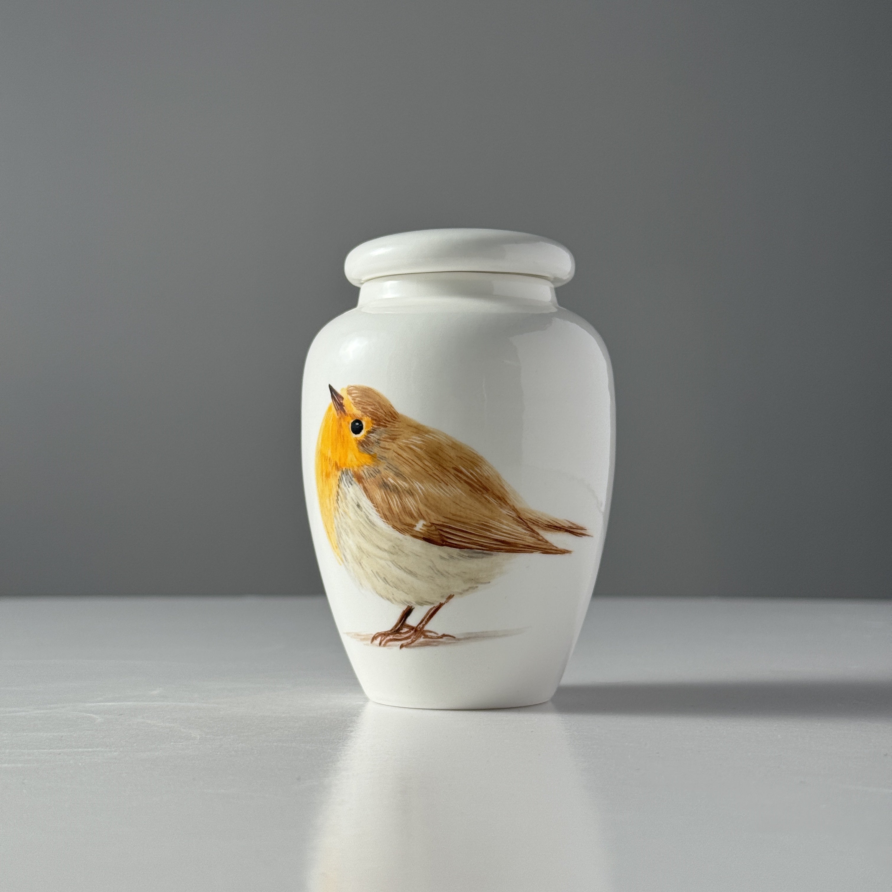 White urn with a robin design on a gray background