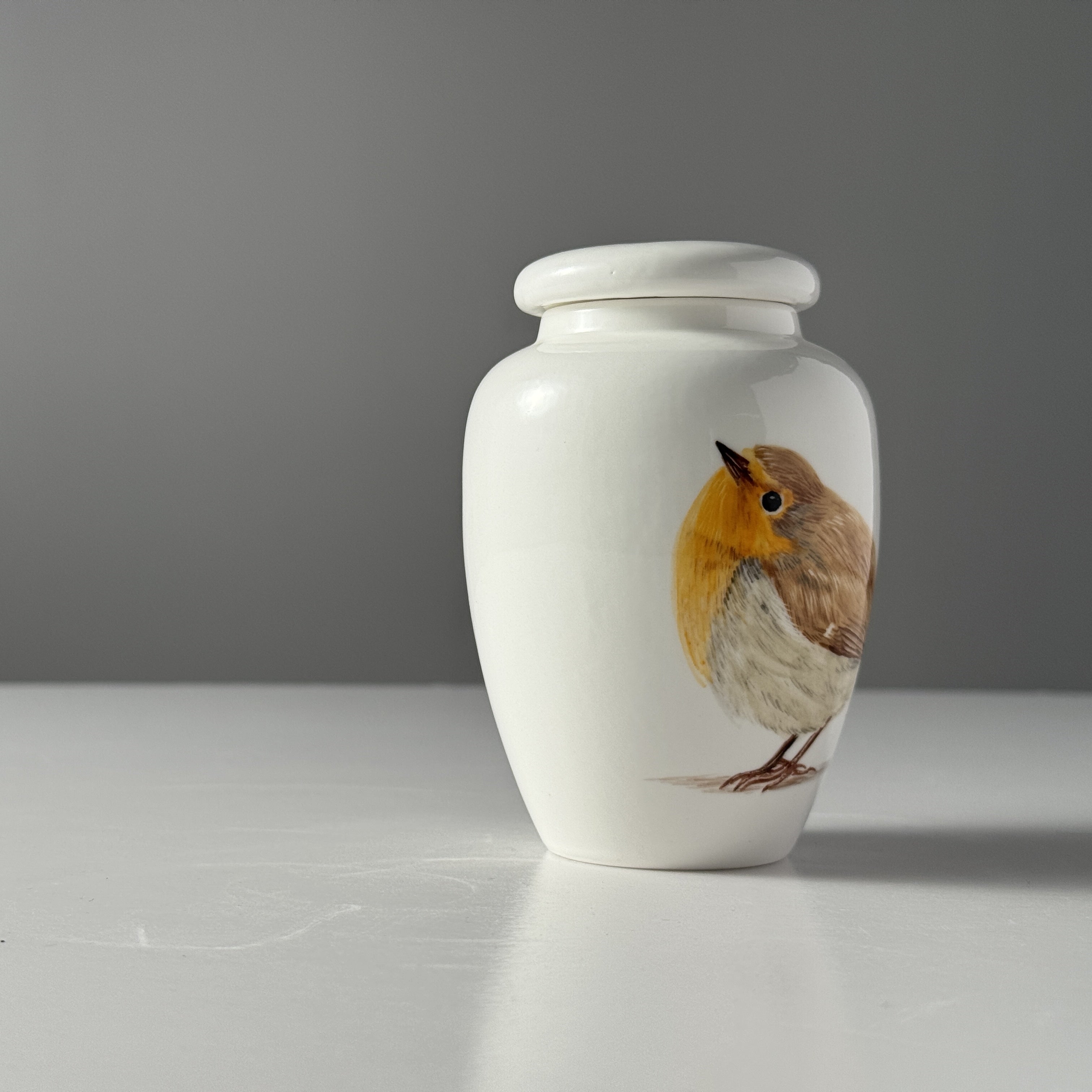 White urn with a painted bird design on a gray background