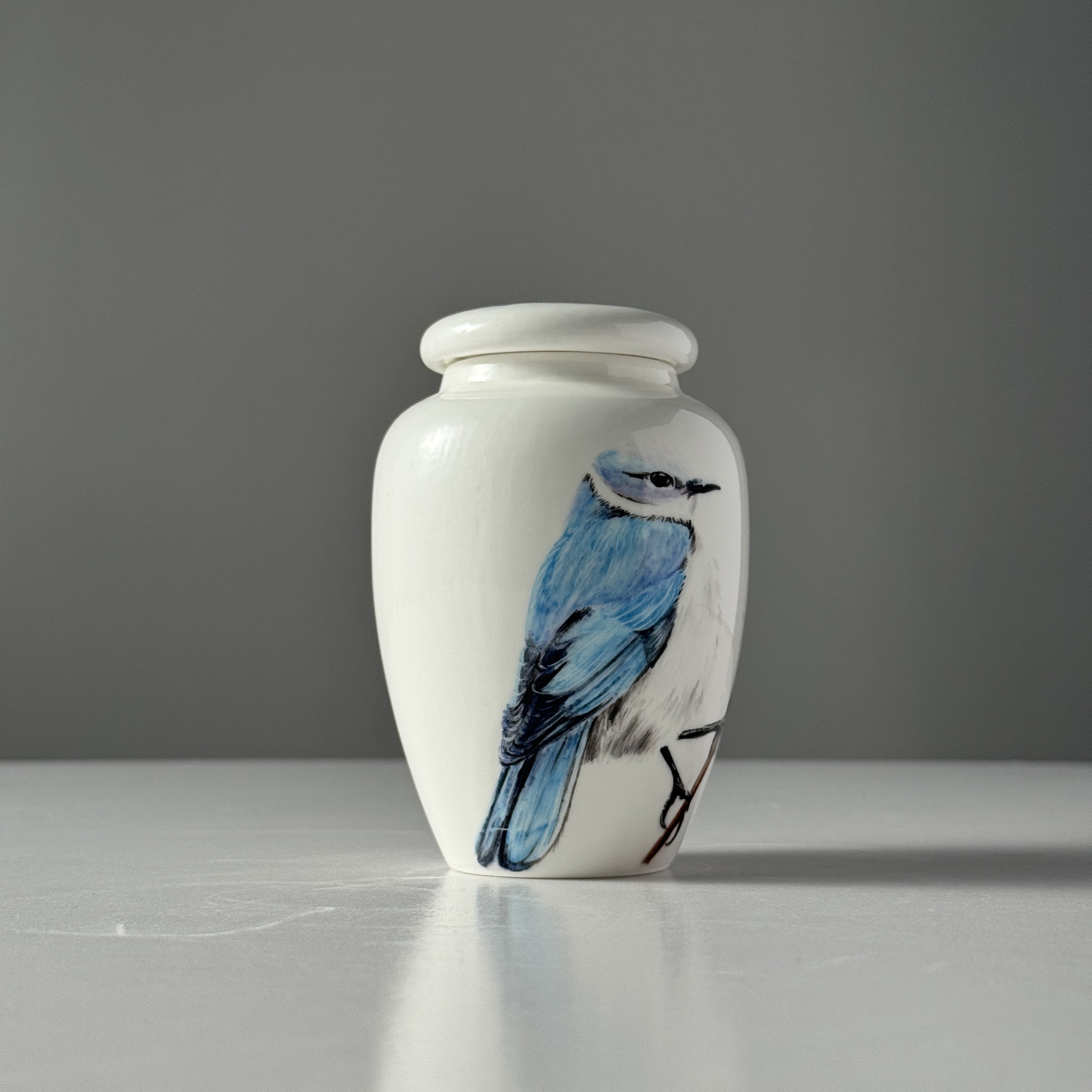 White urn with a blue bird design on a gray background